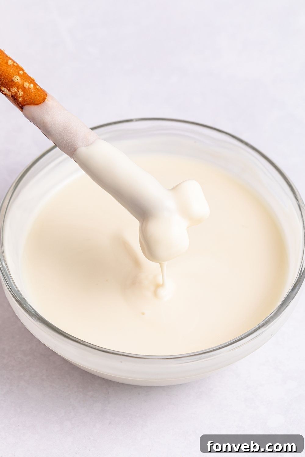 Festive Rice Krispie Drumsticks 7 A pretzel rod being carefully dipped into a bowl of smooth, melted white chocolate, illustrating the coating process.