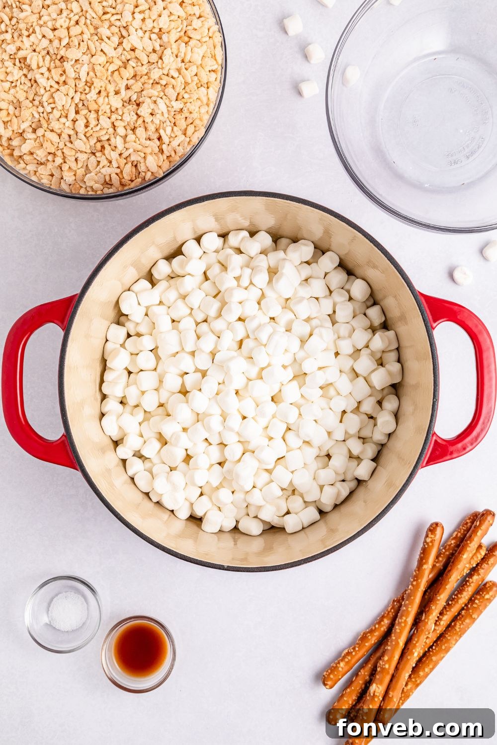 Festive Rice Krispie Drumsticks 9 A large pot filled with mini marshmallows, positioned on a table alongside cereal, pretzels, and other components, awaiting the next step.