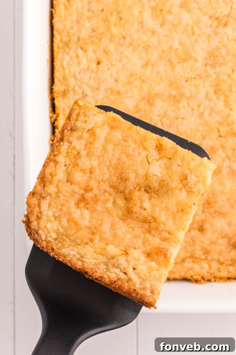 Harvest Pumpkin Pie Delight 11 A slice of Pumpkin Pie Cake carefully lifted from the pan with a spatula, showcasing its distinct layers, with the rest of the cake still in the pan.