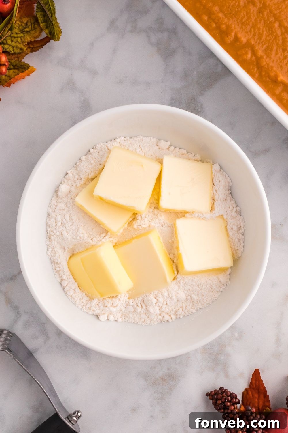 Harvest Pumpkin Pie Delight 5 Butter and cake mix in a mixing bowl on a table, with a raw cake base in a pan to the side, ready for preparation.