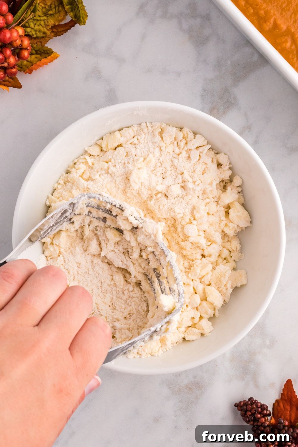 Harvest Pumpkin Pie Delight 6 A pastry cutter actively crumbling together butter and cake mix in a bowl, showing the texture of the crumb topping in progress.