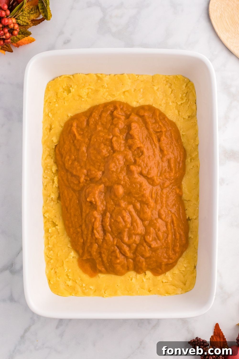 Harvest Pumpkin Pie Delight 7 The raw pumpkin pie filling evenly spread over the cake crust in a baking pan, sitting on a table, ready for the next layer.