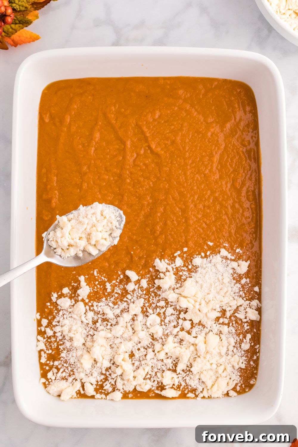 Harvest Pumpkin Pie Delight 8 A spoon gently sprinkling the prepared crumb topping over the smooth raw pumpkin pie filling in the baking pan, preparing for baking.