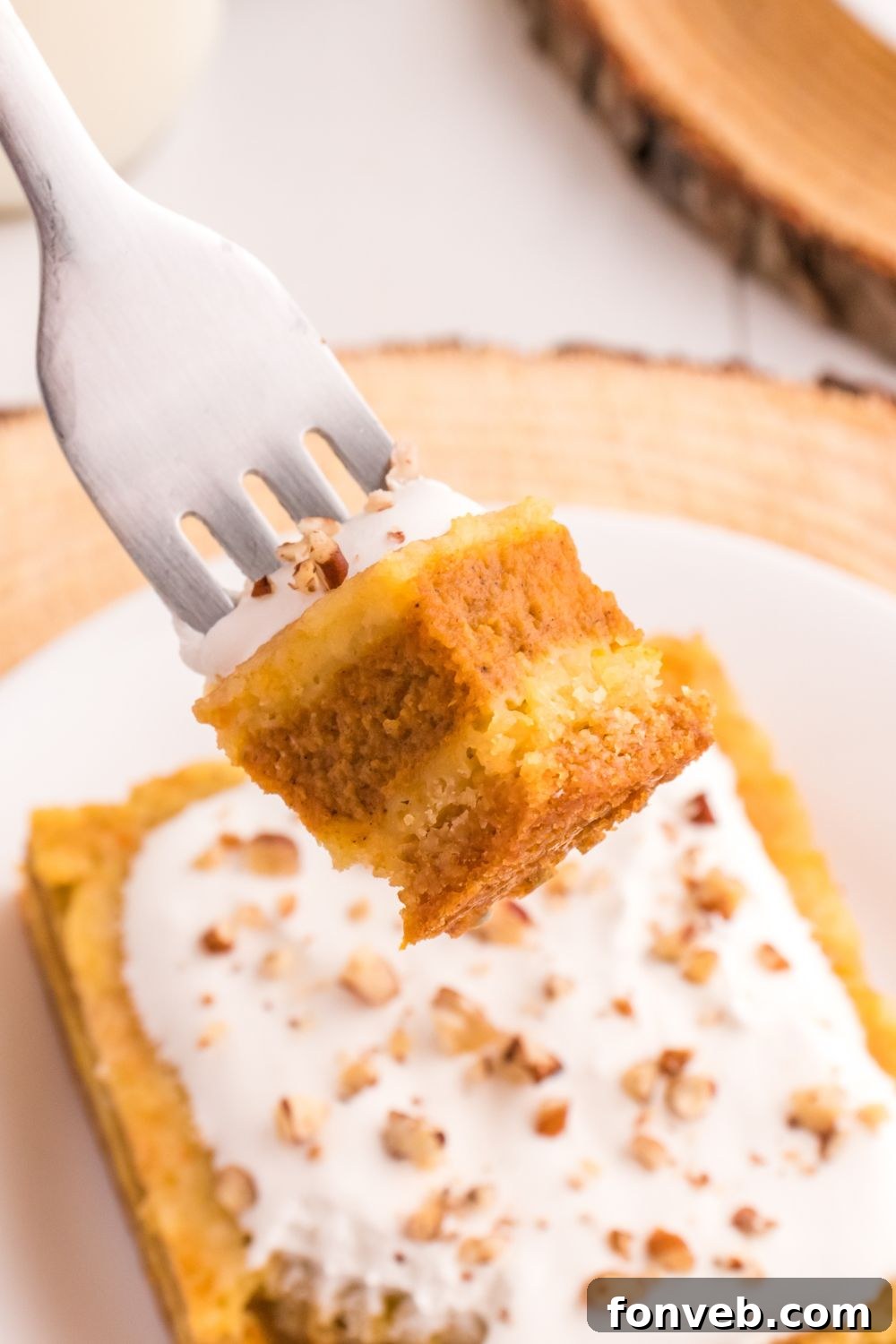 Harvest Pumpkin Pie Delight 10 A pristine slice of Pumpkin Pie Cake sits on a white plate, with a fork poised, carrying a small, perfect bite of the layered dessert, ready to be enjoyed.