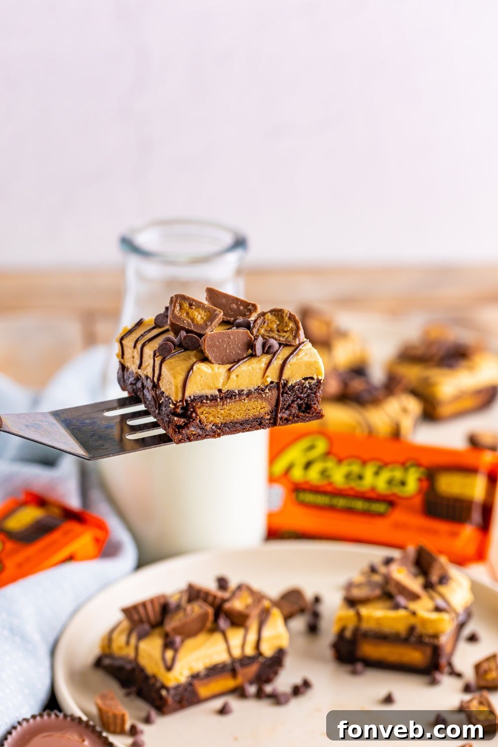 A spatula holding a single peanut butter cup brownie, elevated above a table where more brownies are neatly sliced and presented on a plate