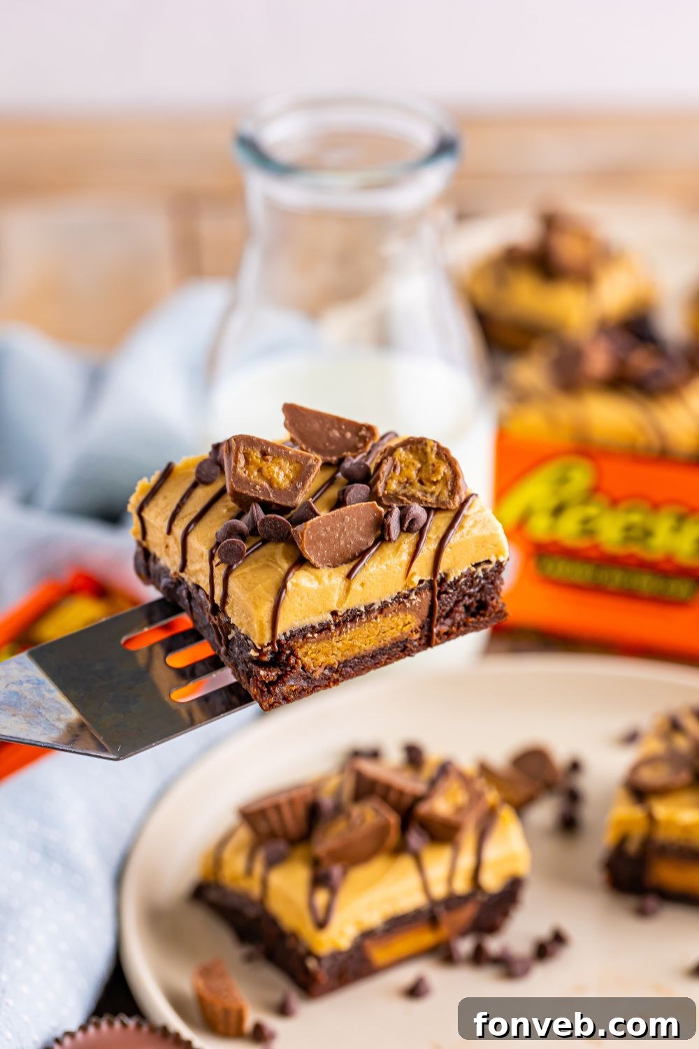 A single Reese's Stuffed Brownie lifted on a spatula, showcasing its thick frosting and rich chocolate layers, with more brownies on the table below