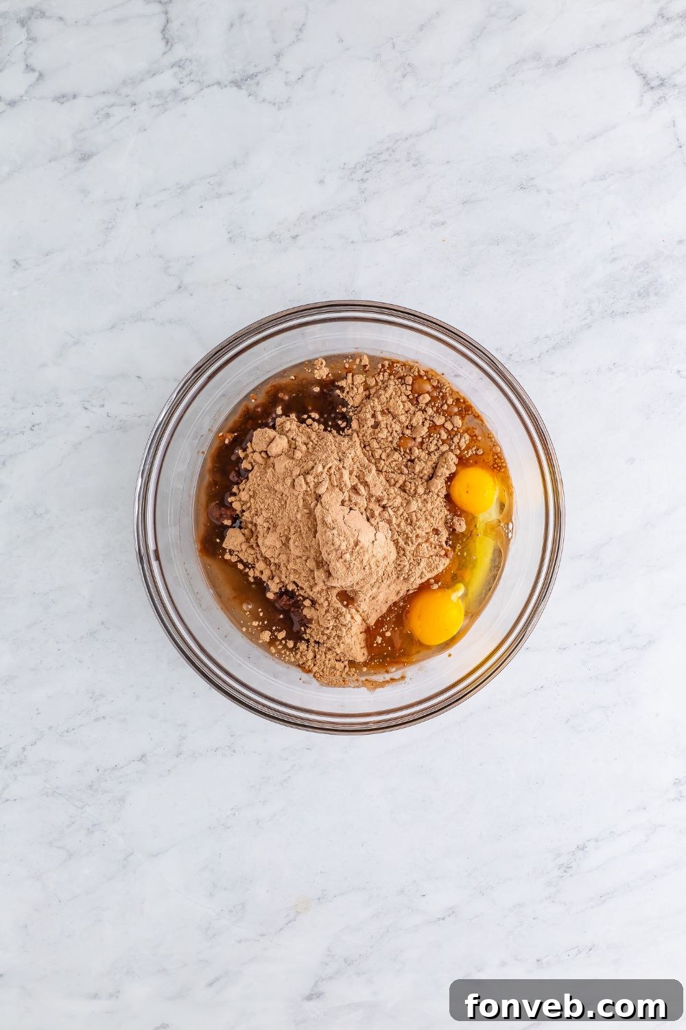 A bowl containing brownie mix, with an egg and oil visibly placed to the sides, ready to be combined into batter