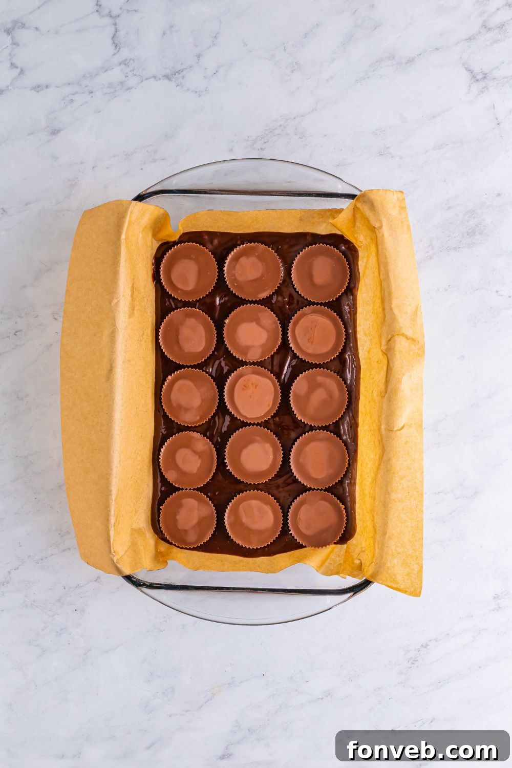 An overhead shot of brownie mix in a casserole dish, generously topped with an array of Reese's Peanut Butter Cups, ready for baking