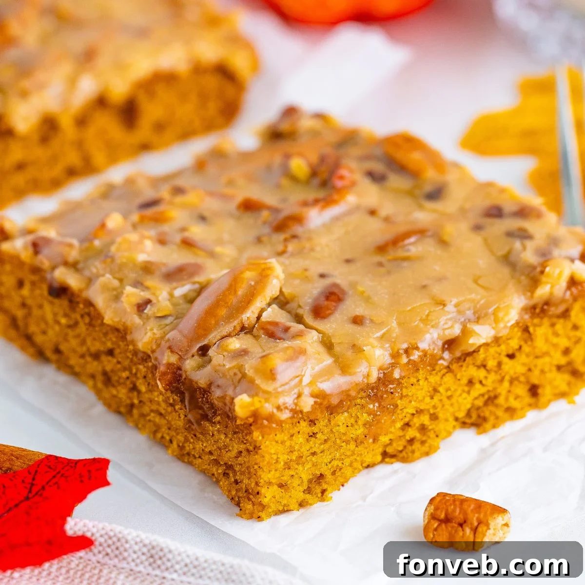 A perfectly sliced piece of Pumpkin Snack Cake with Praline Icing, showcasing its moist texture and crunchy topping, resting on a napkin atop a rustic wooden table.