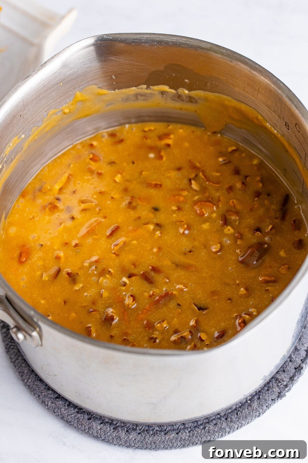 A metal pan filled with decadent praline pecan icing, thick and ready to be spread, sitting on a kitchen counter.