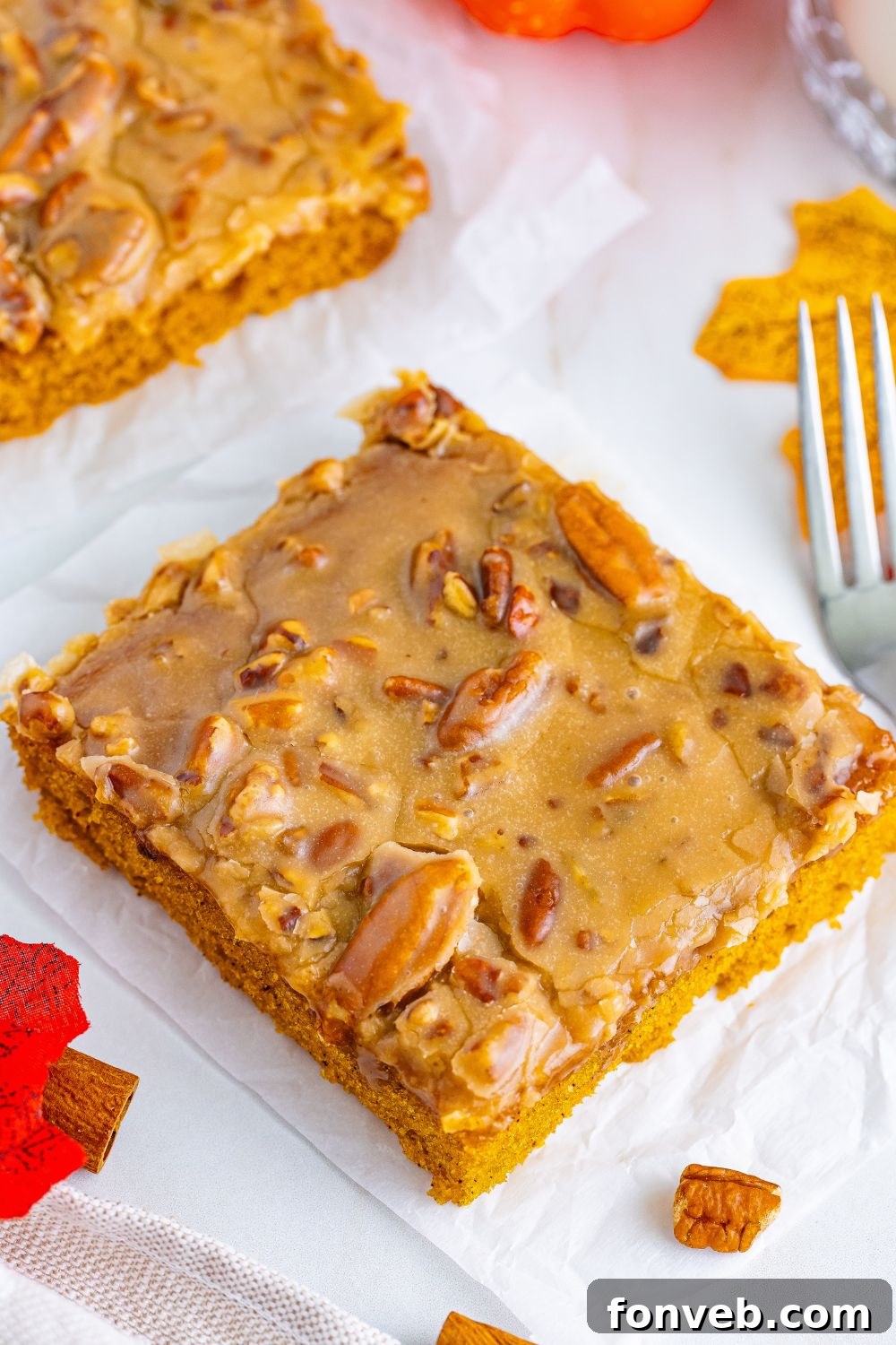 Square slices of Pumpkin Snack Cake with Praline Icing arranged on a table, garnished with a few scattered pecans and a fork, highlighting its inviting texture.