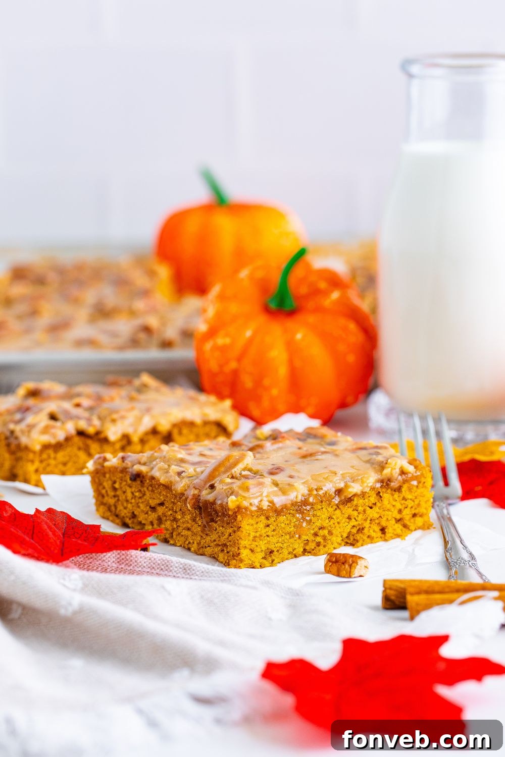 A slice of Pumpkin Snack Cake with Praline Icing on a plate, alongside a glass of milk, with the remaining cake in its pan visible in the background, creating a complete dessert scene.