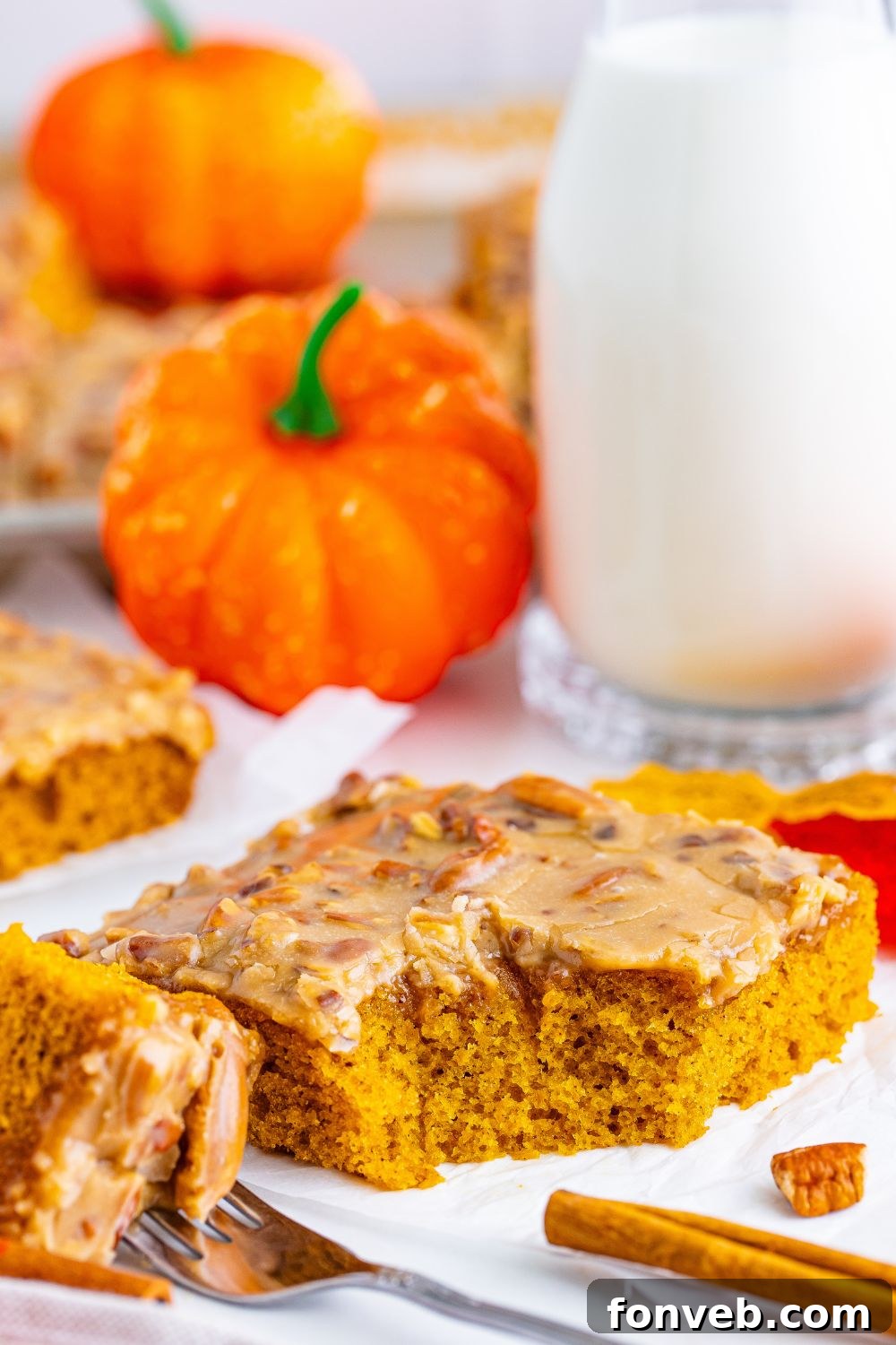 A slice of pumpkin snack cake on a plate with a fork and a cinnamon stick, creating an inviting fall dessert scene.