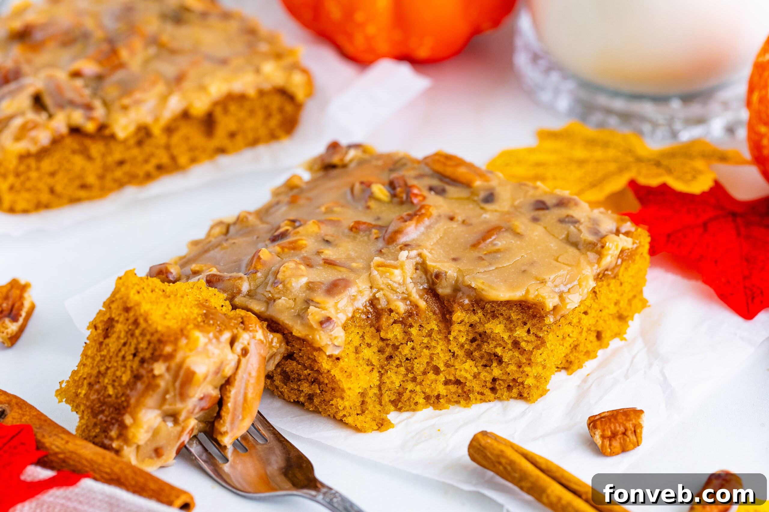 A slice of Pumpkin Snack Cake with Praline Icing on a plate, with a fork holding a bite, set on a beautifully decorated fall table.