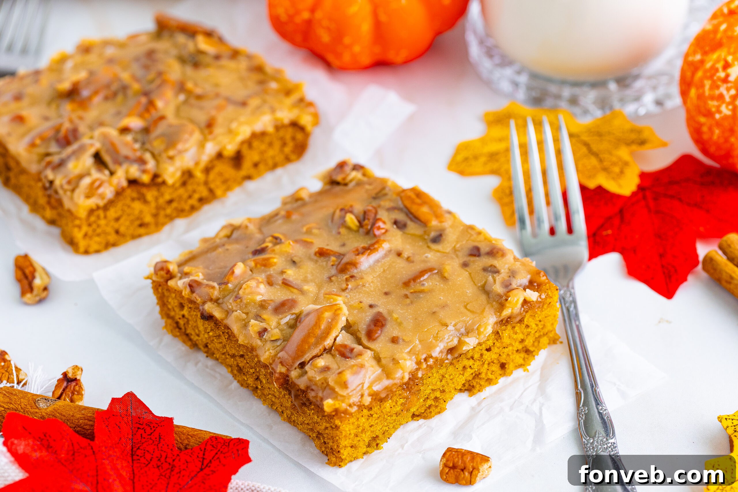 Multiple slices of Pumpkin Snack Cake with Praline Icing arranged on a white serving platter, surrounded by vibrant fall leaves, creating a festive autumn display.