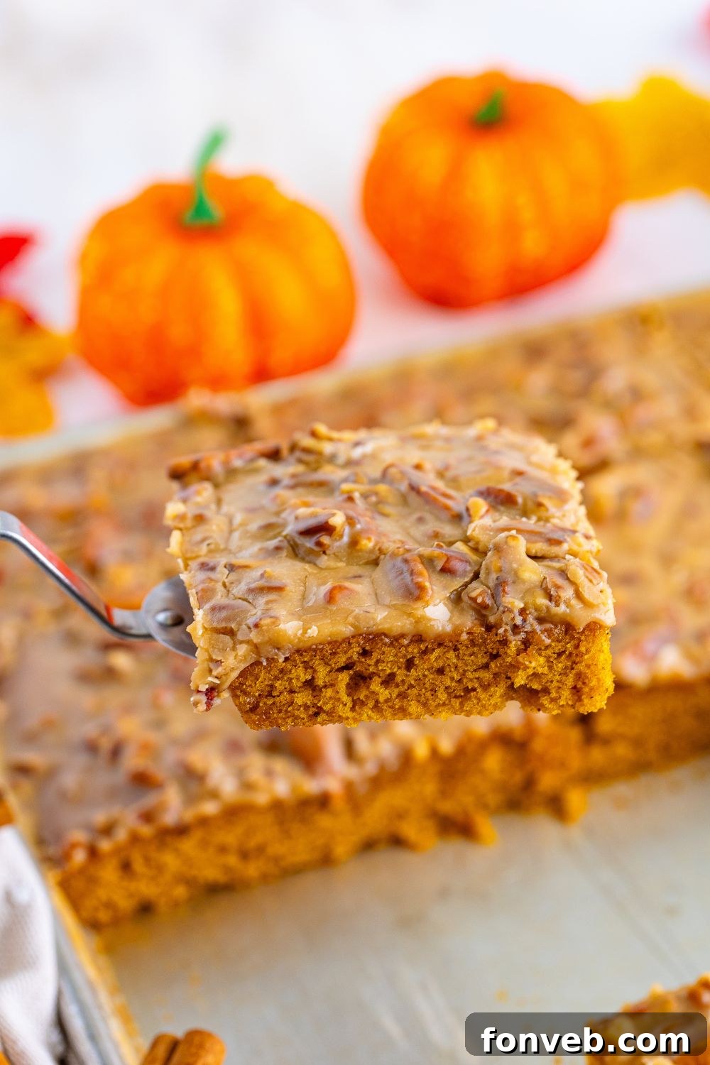 A Pumpkin Snack Cake with Praline Icing in a baking pan, with a spatula lifting a generous slice, ready to be served.