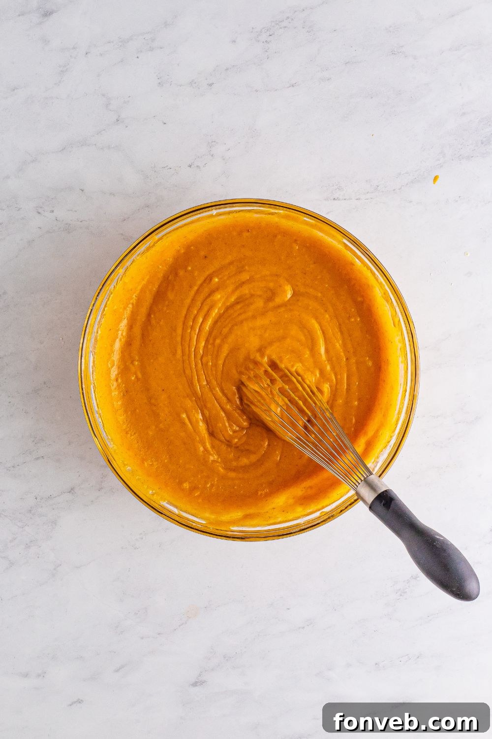A glistening glass bowl filled with rich pumpkin cake batter, a whisk resting inside, ready for baking.