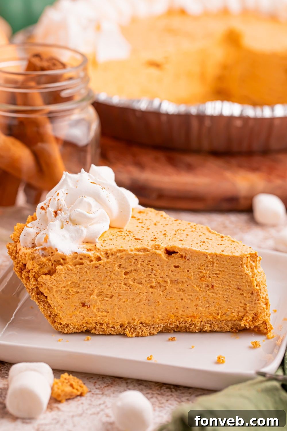 Slice of Marshmallow Pumpkin Pie on plate with the rest of the pie behind it on table 