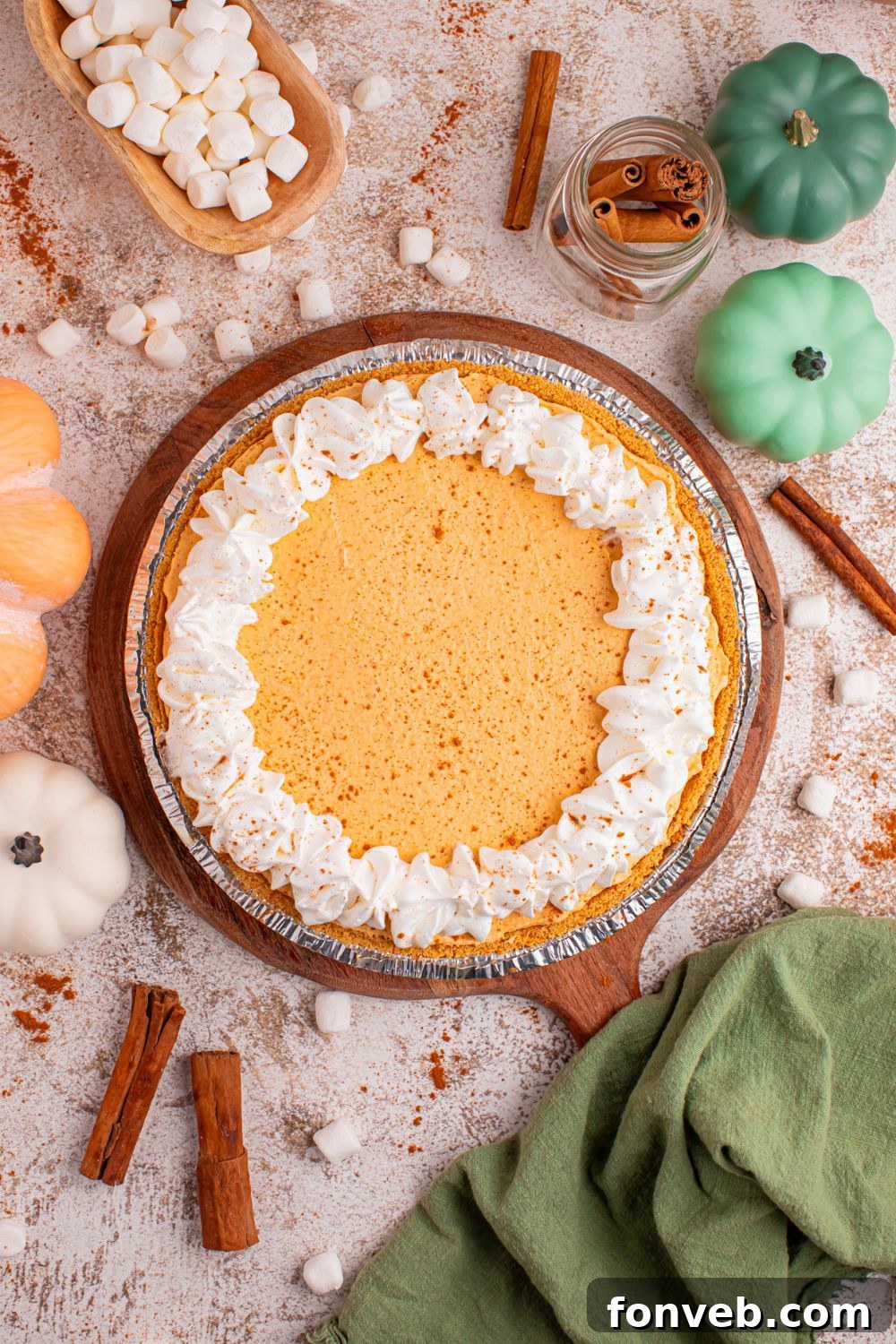 Marshmallow Pumpkin Pie on table with mini marshmallows, fall decor, cinnamon sticks and more around the pie on table 
