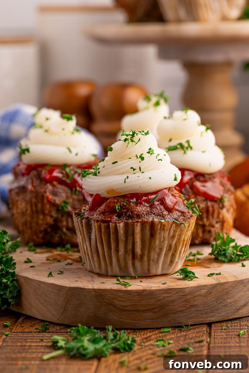 Meatloaf Cupcakes on a wooden cutting board on table with a tray of meatloaf cupcakes in background 