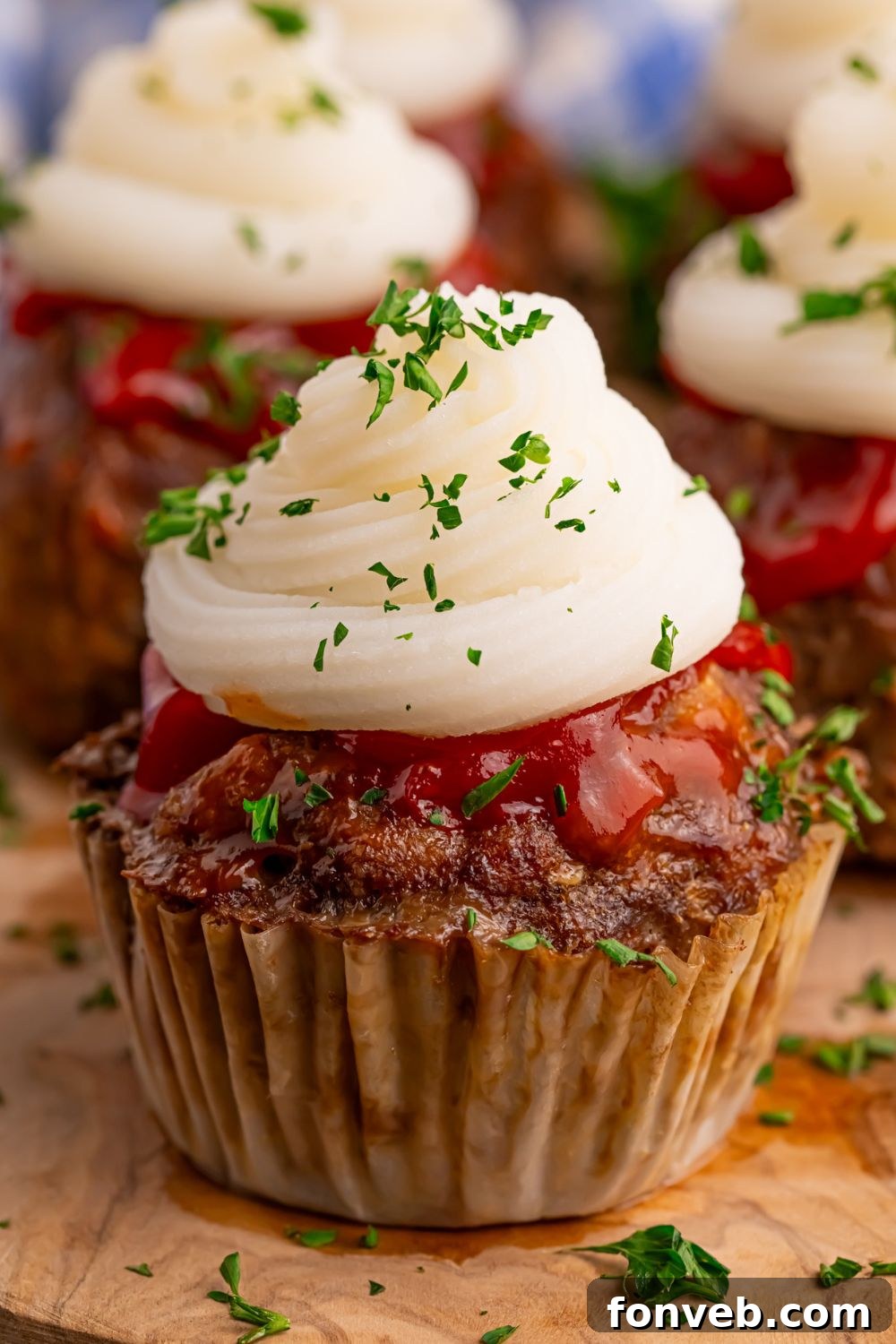 Meatloaf Cupcakes on table with a cupcake liner on them and fresh herbs sprinkled on top of each cupcake