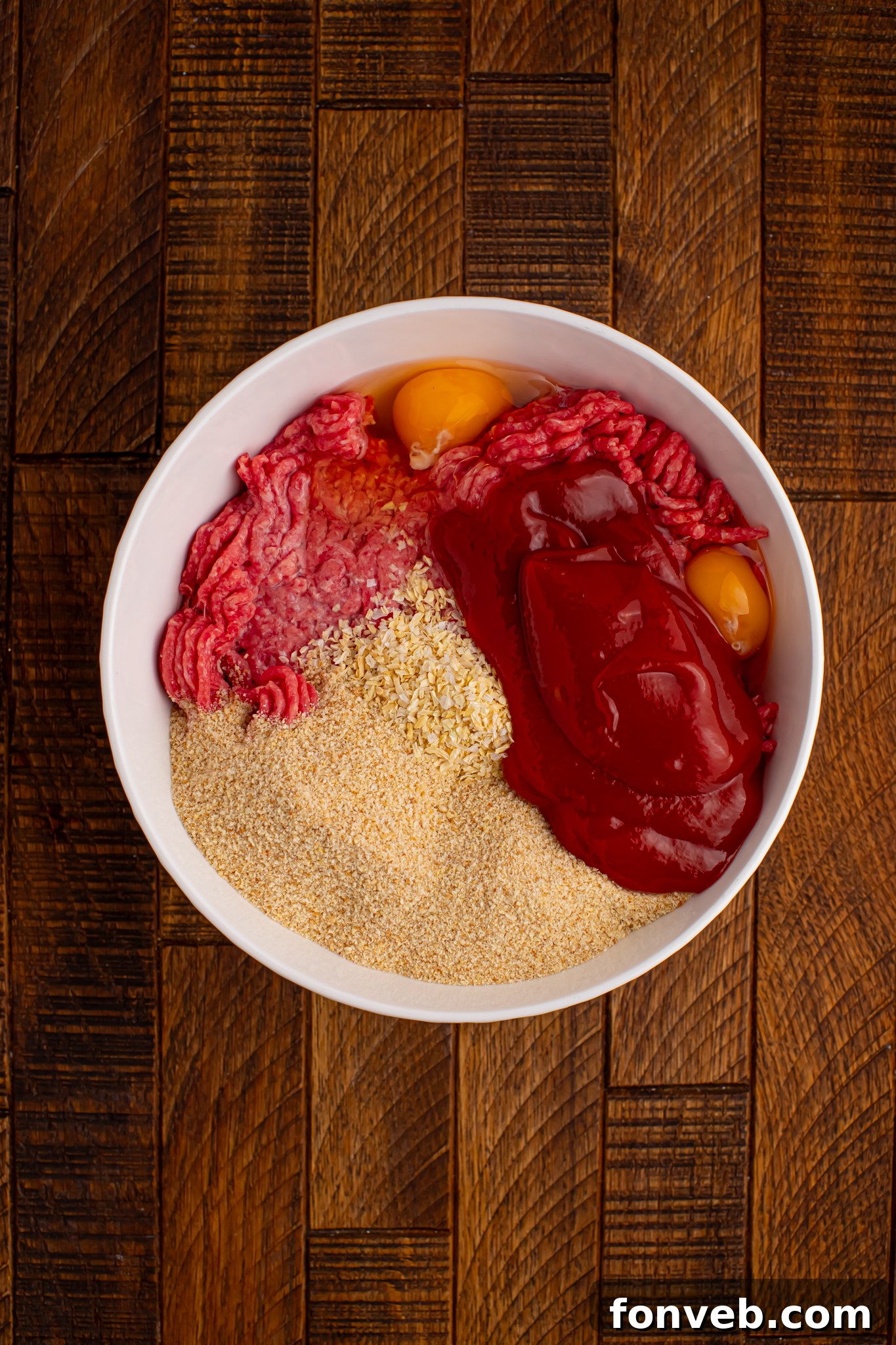 meatloaf ingredients in a white bowl sitting on a wood table 