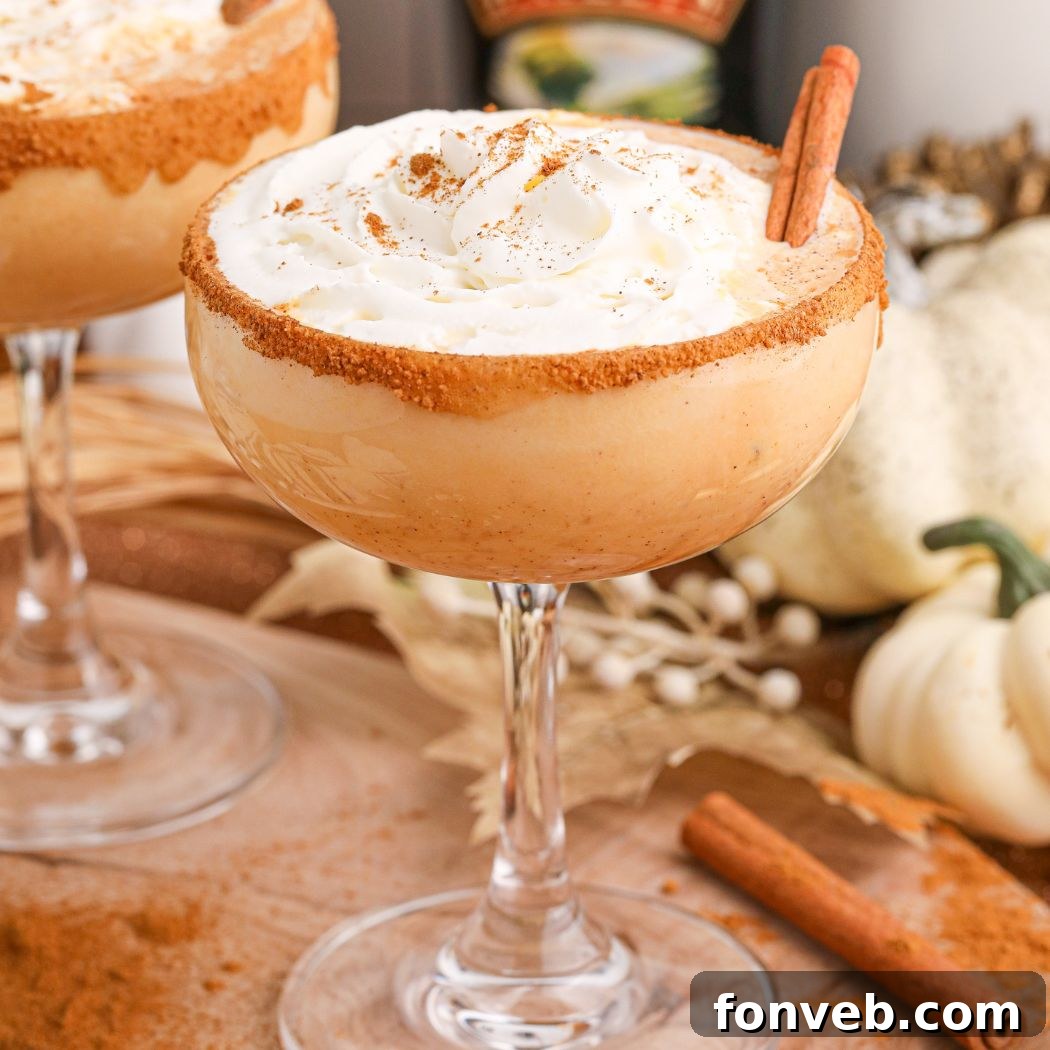 A beautifully presented Pumpkin Pie Martini, with a cinnamon stick garnish, sits on a table adorned with fall holiday decorations, highlighting its seasonal appeal.