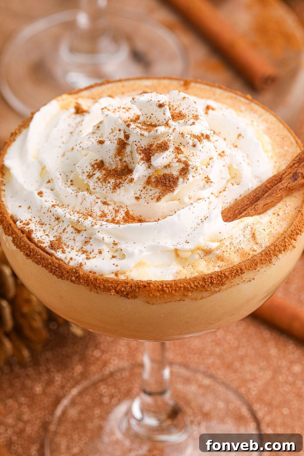 A close-up view of a Pumpkin Pie Martini in a glass, generously topped with whipped cream and a sprinkle of spice, emphasizing its decadent nature.