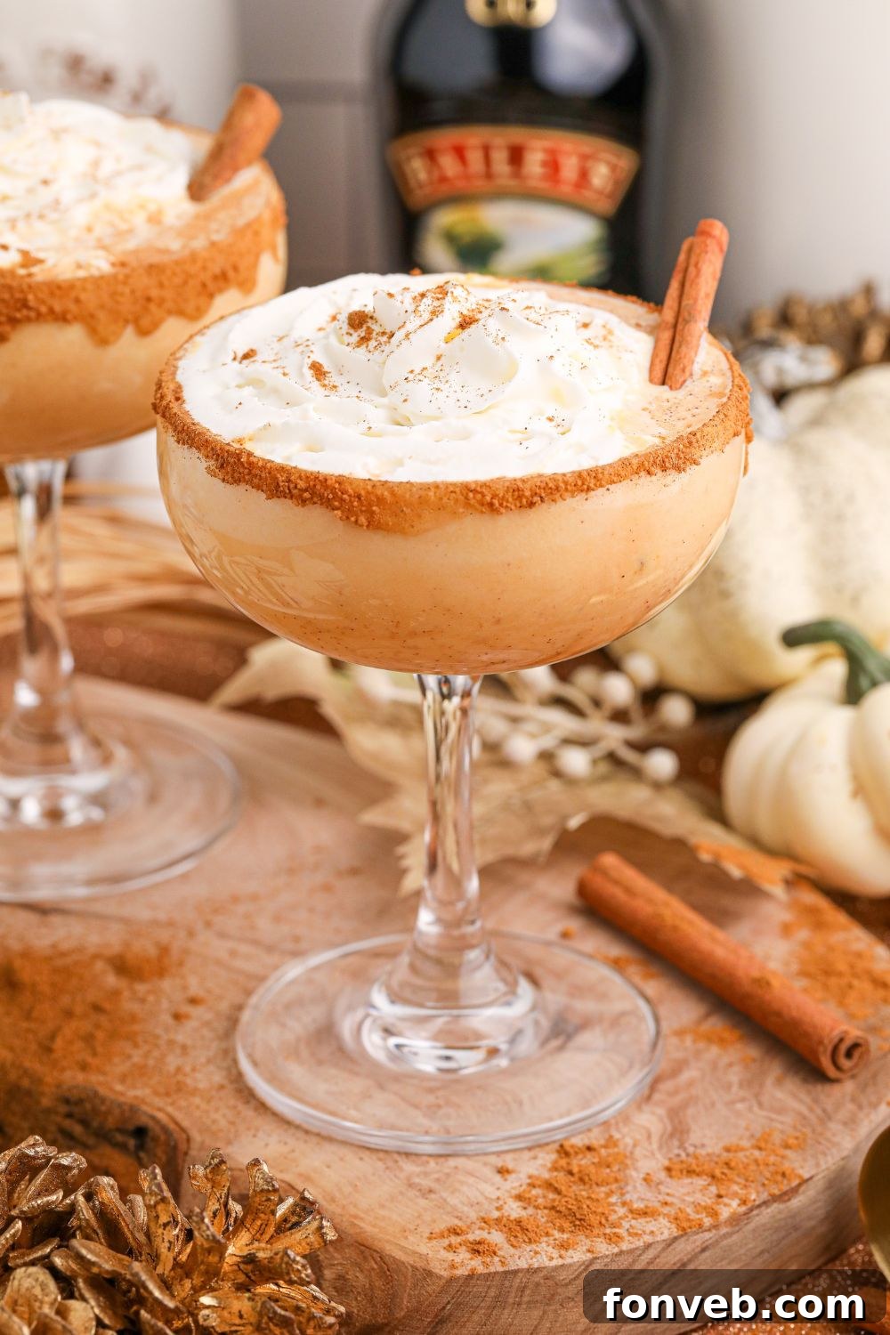 Multiple Pumpkin Pie Martinis are arranged on a table, with bottles of various alcohols in the background, suggesting the ingredients used to create them.