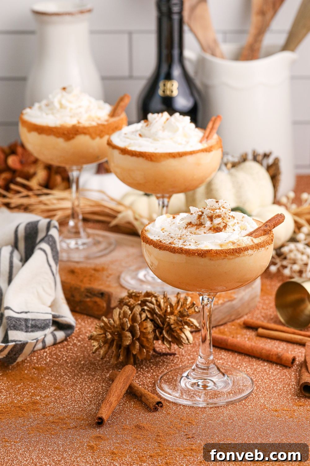 Glasses of pumpkin martinis are showcased on a table adorned with fall decor, with bottles of alcohol in the background, illustrating the drink's festive setting and ingredients.