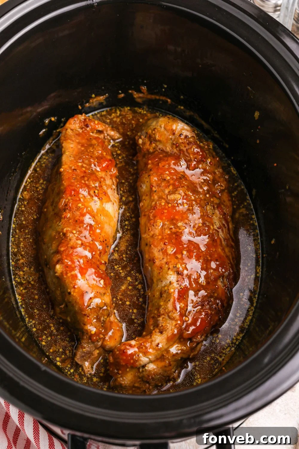 two pork tenderloins in a slow cooker with apricot preserves sauce poured over the meat 