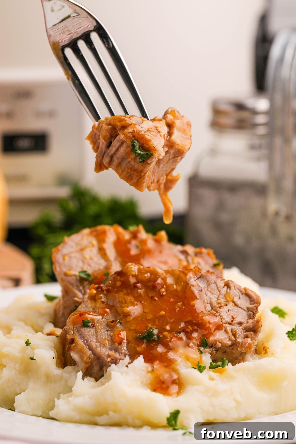 Crock Pot Apricot Pork Tenderloin sliced and placed on a plate with mashed potatoes and a fork with a bite of pork on it 
