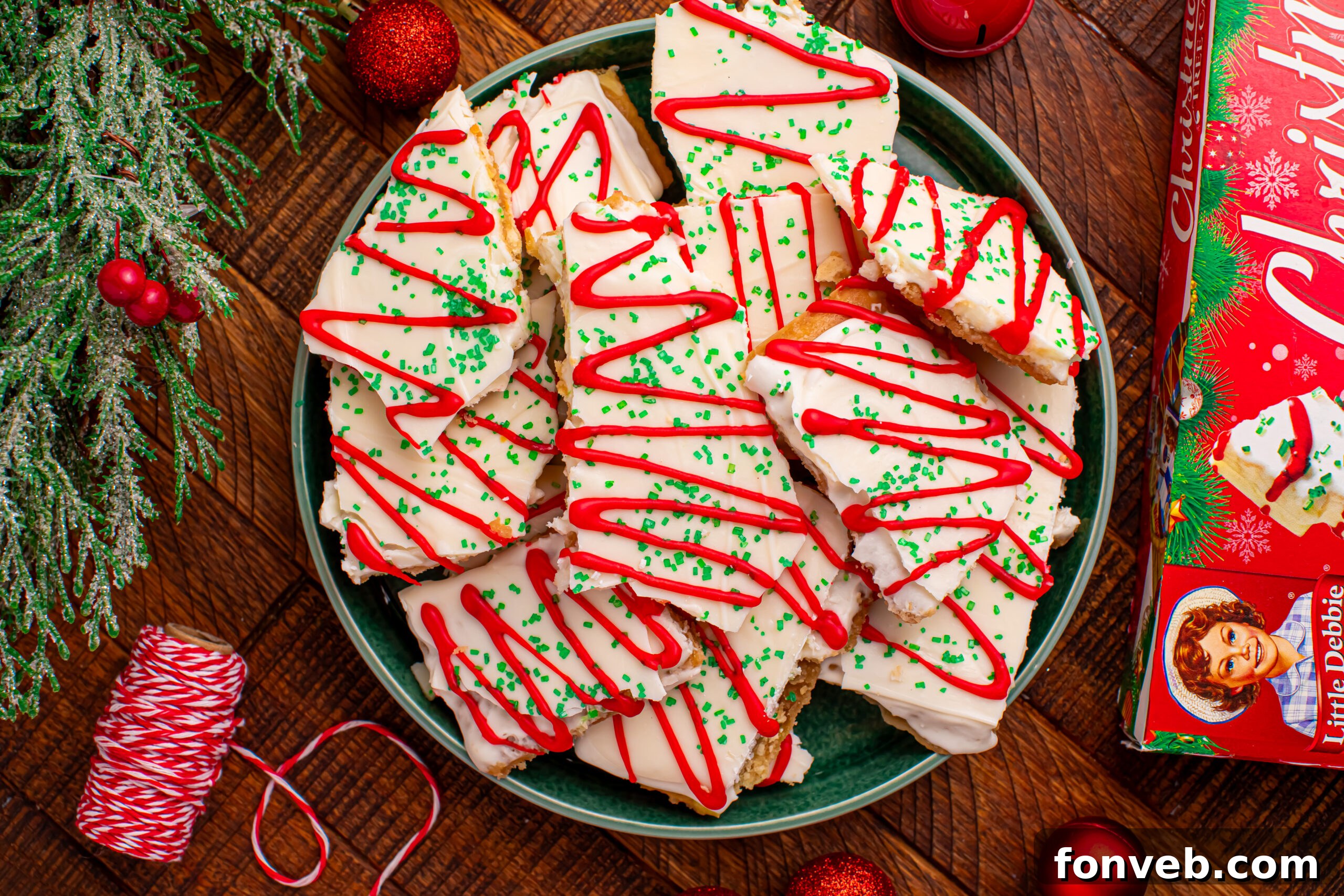 Addictive Little Debbie Christmas Tree Cake Toffee Bark 16 Overhead shot of the Christmas Tree Crack piled on a green serving platter on a dark wood table surrounded by christmas decorations
