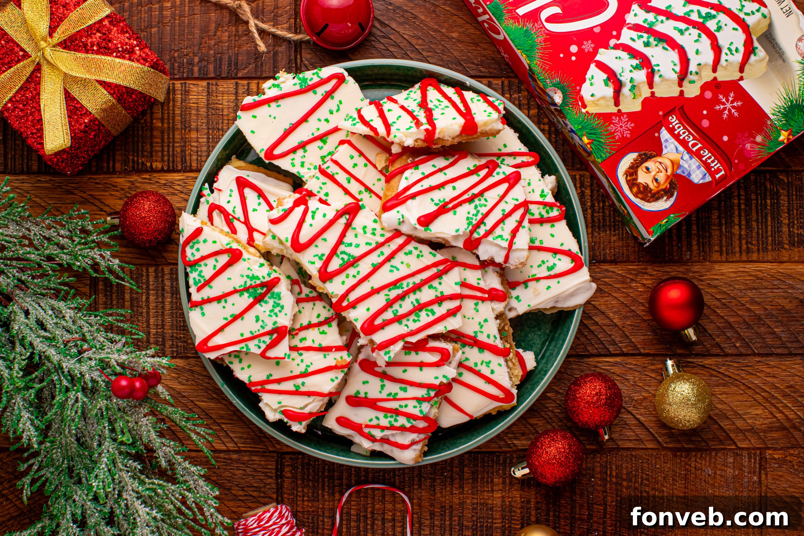 Addictive Little Debbie Christmas Tree Cake Toffee Bark 19 Overhead photo of Christmas Tree Crack piled on a green serving platter on a dark wood table surrounded by christmas decorations