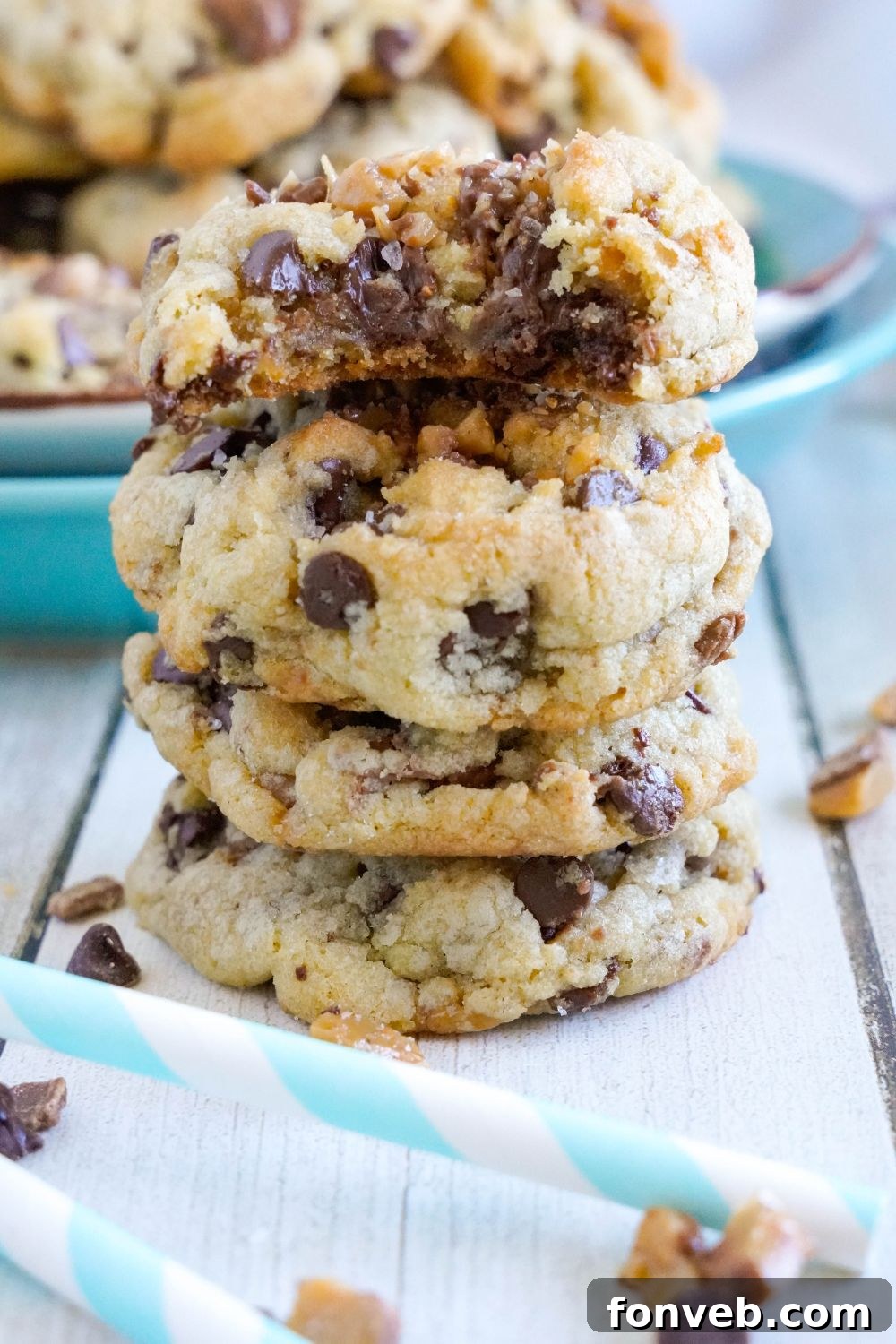 stack of Chocolate Chip Toffee Cookies on table with a plate of cookies behind it 
