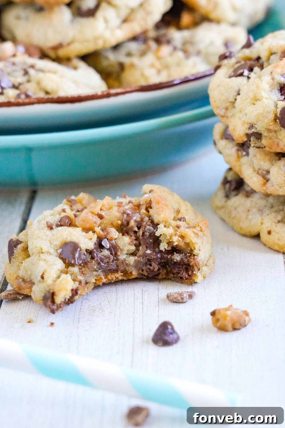 cookie with a bite taken out and a plate of Chocolate Chip Toffee Cookies around table 