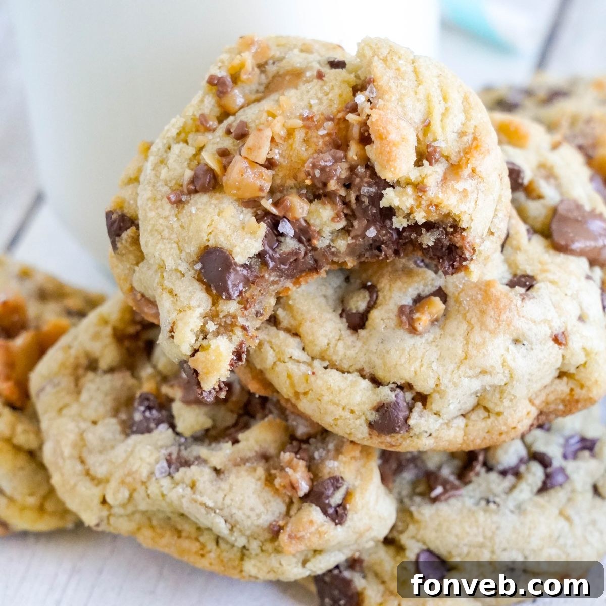 Chocolate Chip Toffee Cookies stacked on top of each other on table with a glass of milk on table 