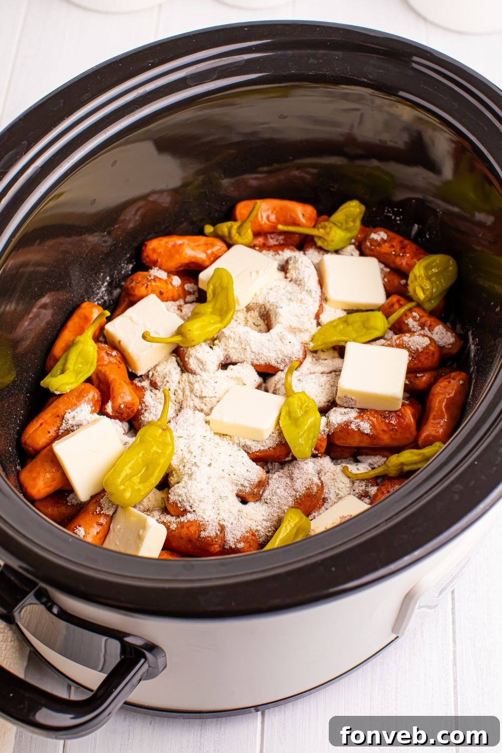 lil smokies in slow cooker with sauce, butter and peppers on top