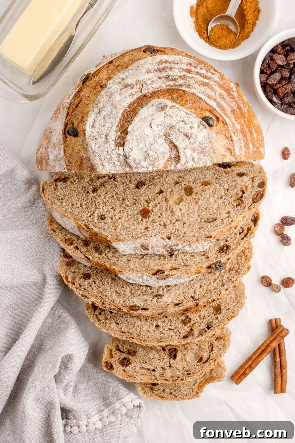 no knead raisin bread sliced and placed on table with cinnamon sticks and raisins around the loaf of bread