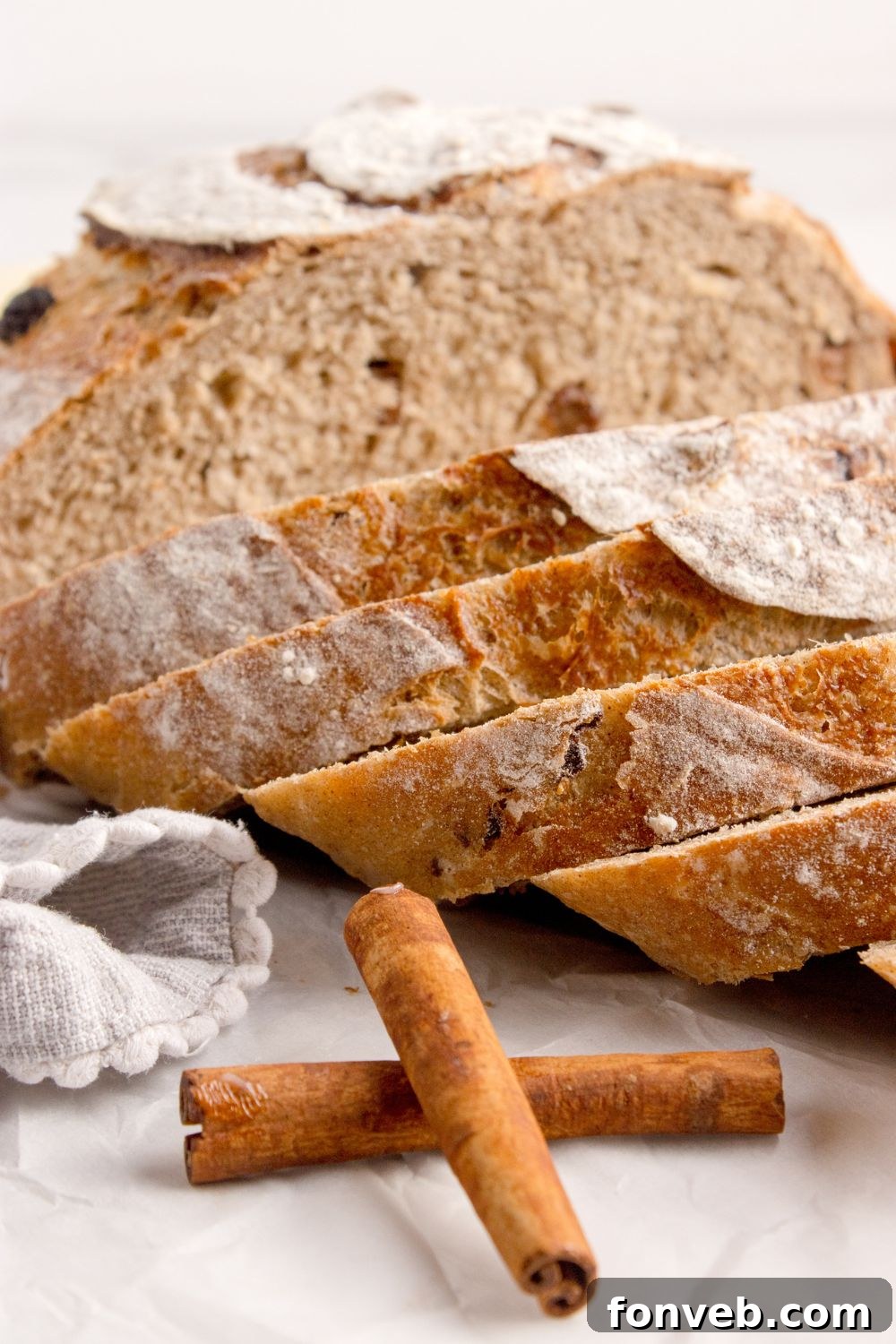 cinnamon raisin dutch oven bread sliced and placed on table with two cinnamon sticks sitting in front of loaf