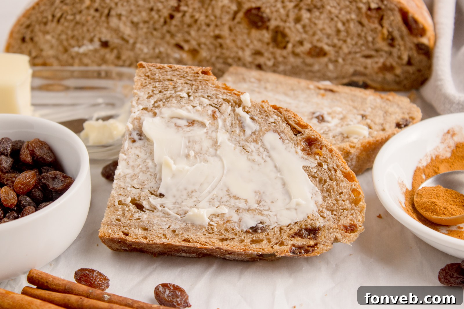 Cinnamon raisin bread on table that is half sliced into slices with one slathered with butter