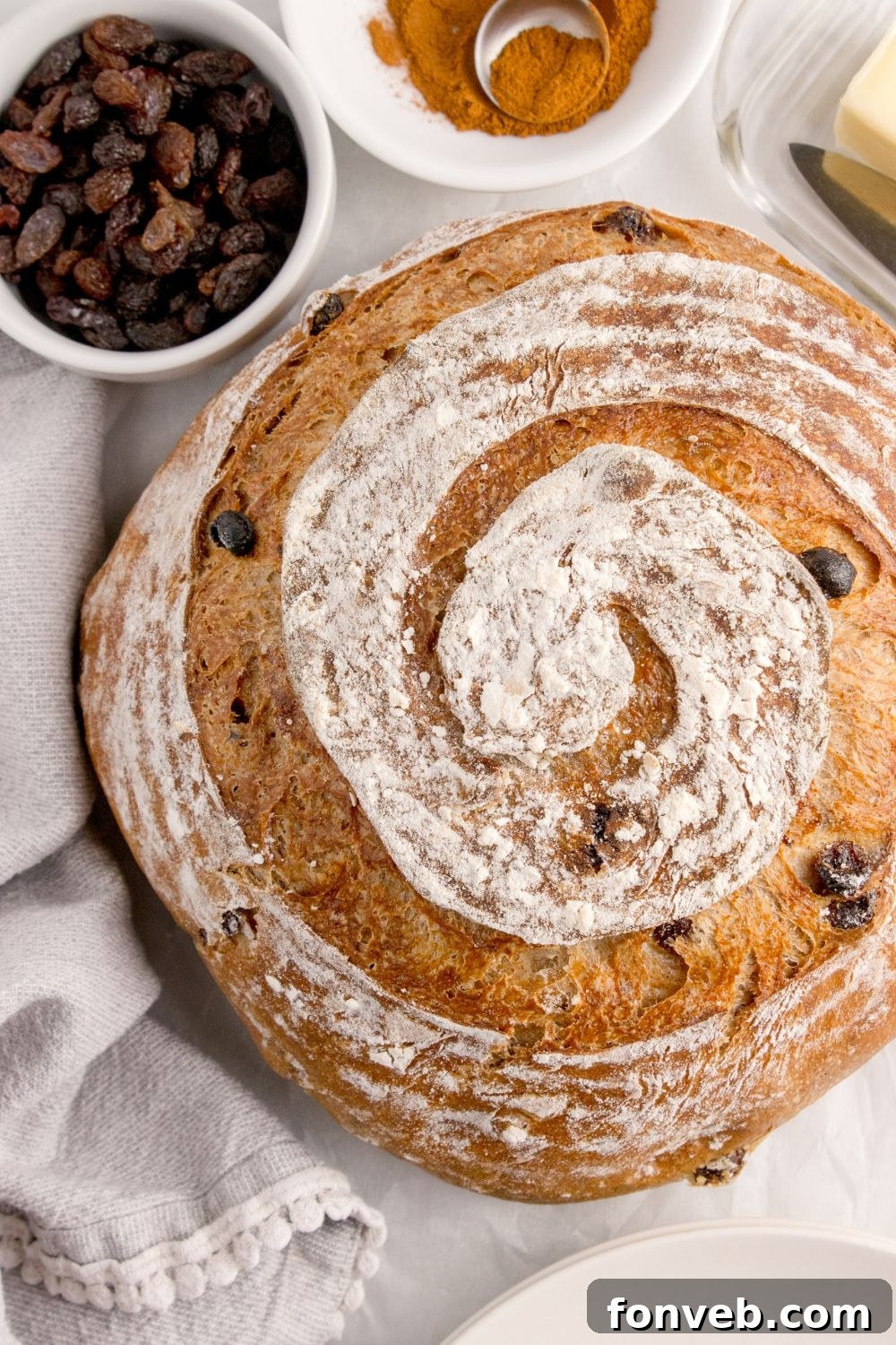 round loaf of cinnamon raisin bread on table with a bowl of raisins behind it