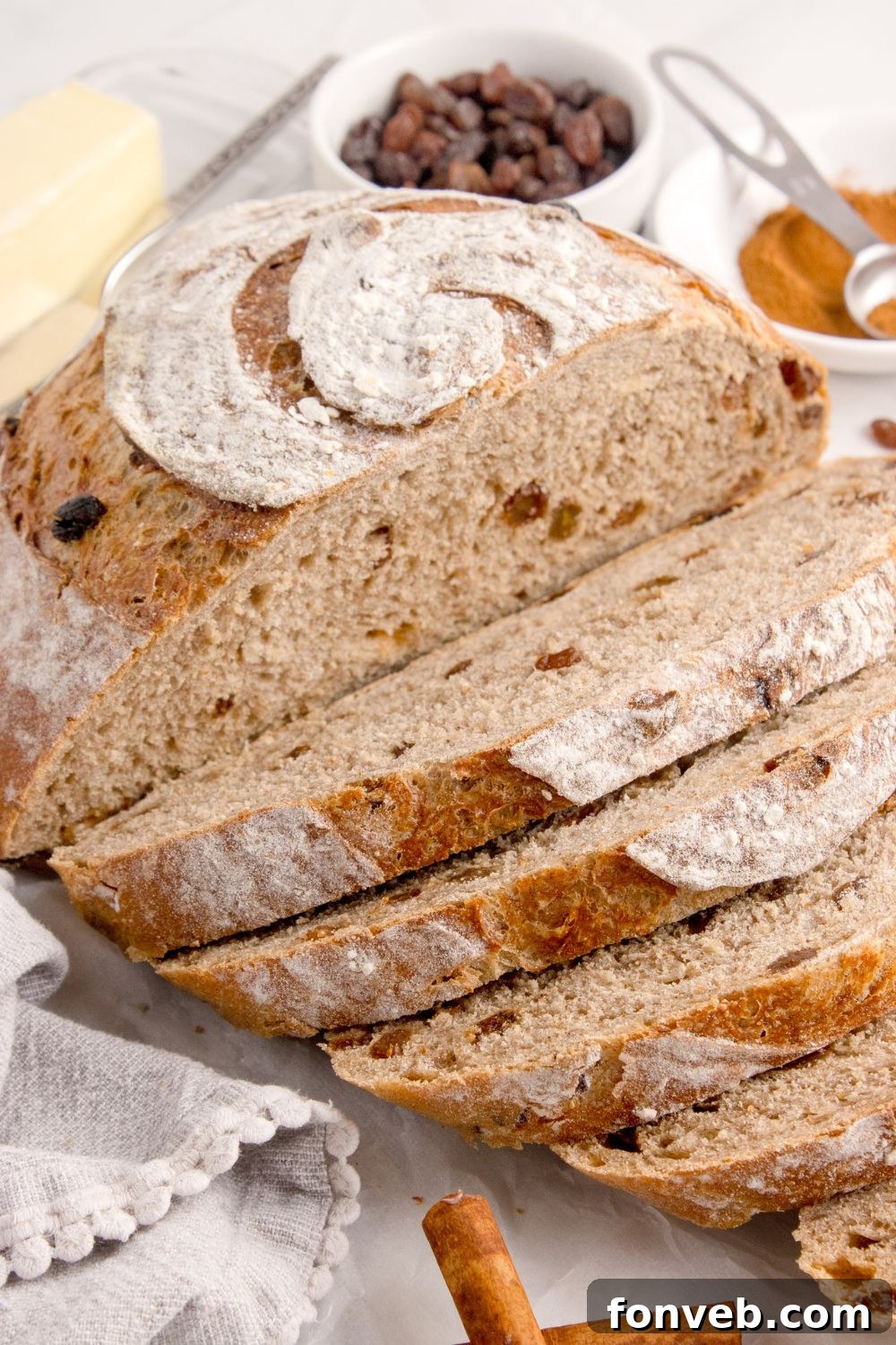 homemade cinnamon raisin bread partly sliced and sitting on table with some raisins in a bowl behind it