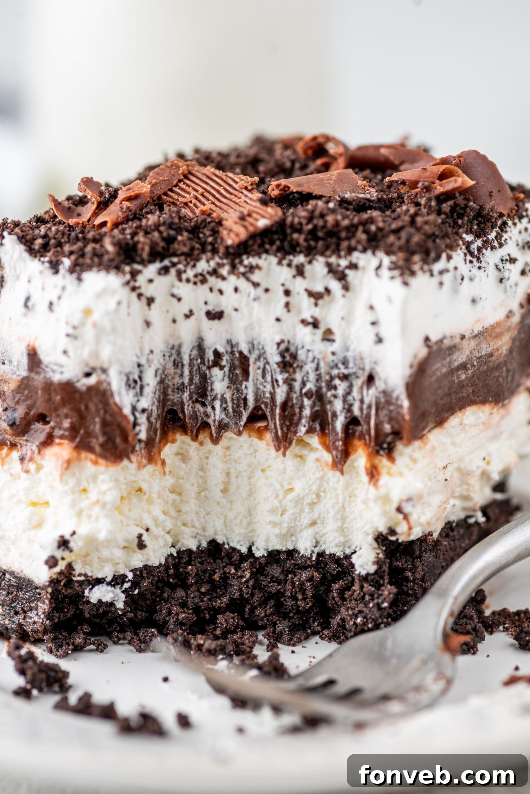 Ultimate Chocolate Oreo Delight 2 Close-up of a slice of Chocolate Oreo Lush, showing the distinct layers of Oreo crust, cream cheese, chocolate pudding, and whipped topping, garnished with Oreo crumbs and chocolate curls.