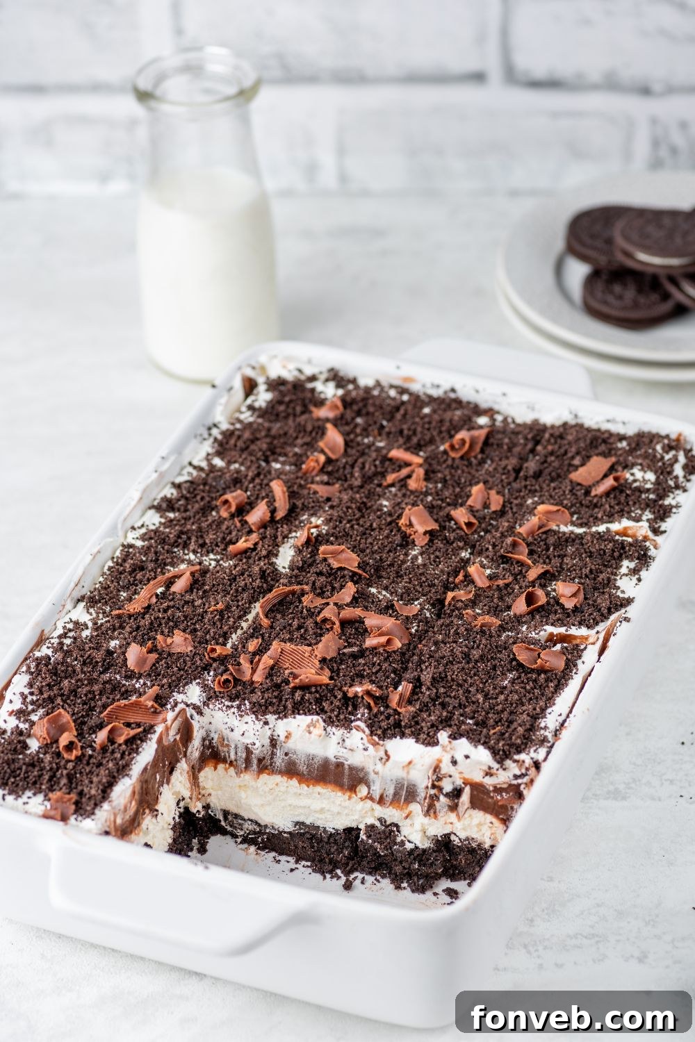 Ultimate Chocolate Oreo Delight 12 A Chocolate Oreo Lush dessert in a casserole pan on a rustic wooden table, with several slices already removed, showing its inviting layers.