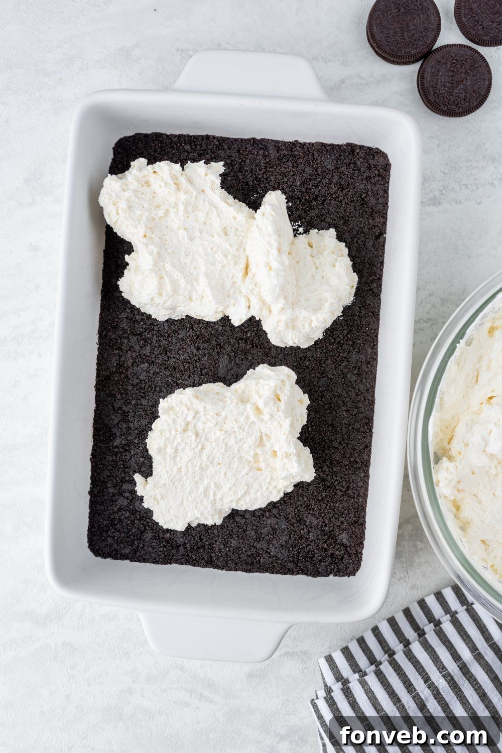 Ultimate Chocolate Oreo Delight 7 The smooth cream cheese layer being carefully spread over the compacted Oreo cookie crust in a baking dish, forming the first creamy layer of the lush dessert.