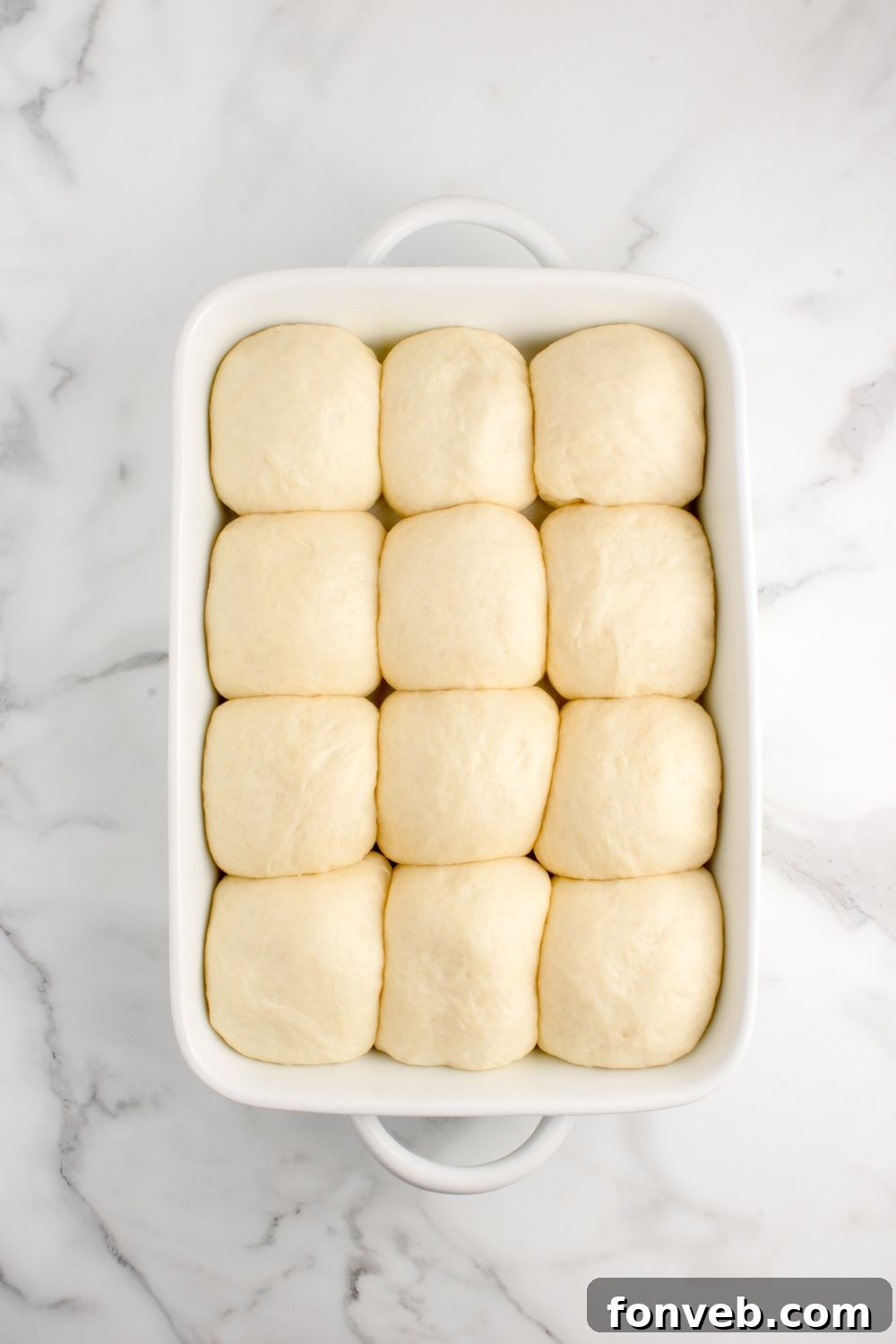 risen dough for rolls in a casserole dish on table