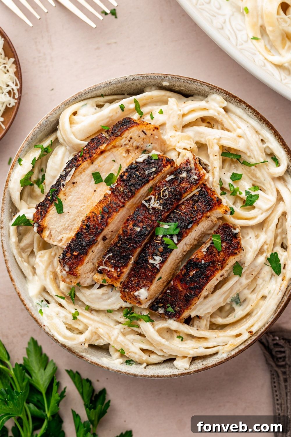 Cajun Chicken Alfredo 17 Blackened Chicken Alfredo in a bowl on table with parsley on the side, forks, and other items around the bowl