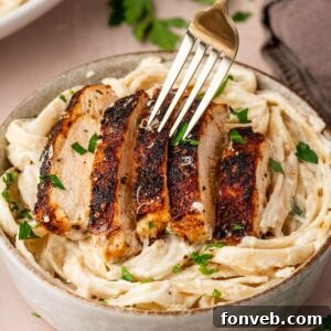 Blackened Chicken Alfredo in a bowl with a fork poking into the chicken