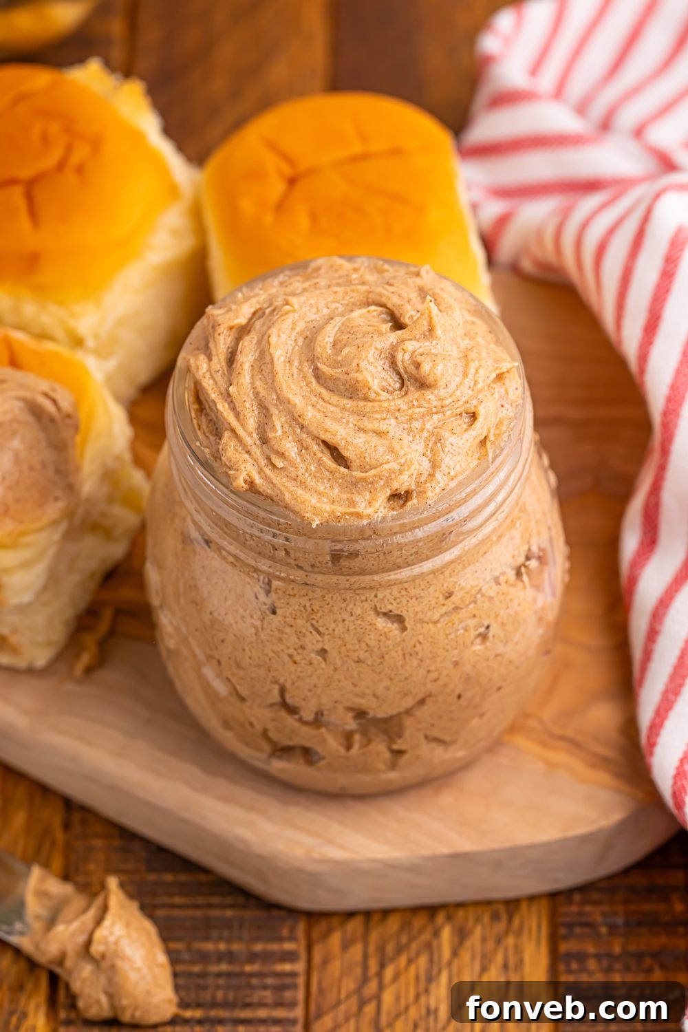 homemade cinnamon butter in a glass jar with rolls around it on table
